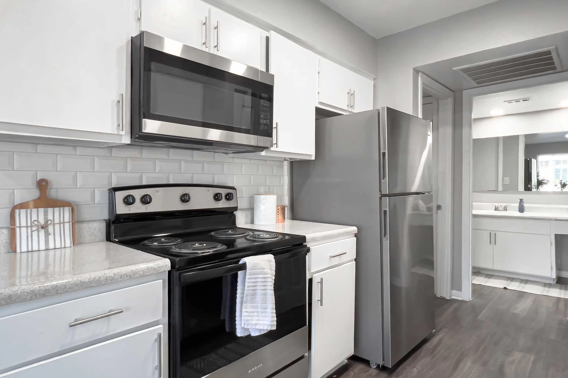 A modern kitchen featuring white cabinets, stainless steel appliances, a black stove, and a grey refrigerator. There are light-colored countertops and a tiled backsplash.
