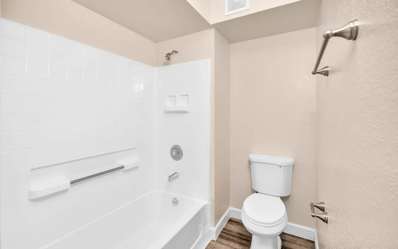 Interior view of a bathroom featuring a bathtub with shower, a toilet, and light-colored walls.