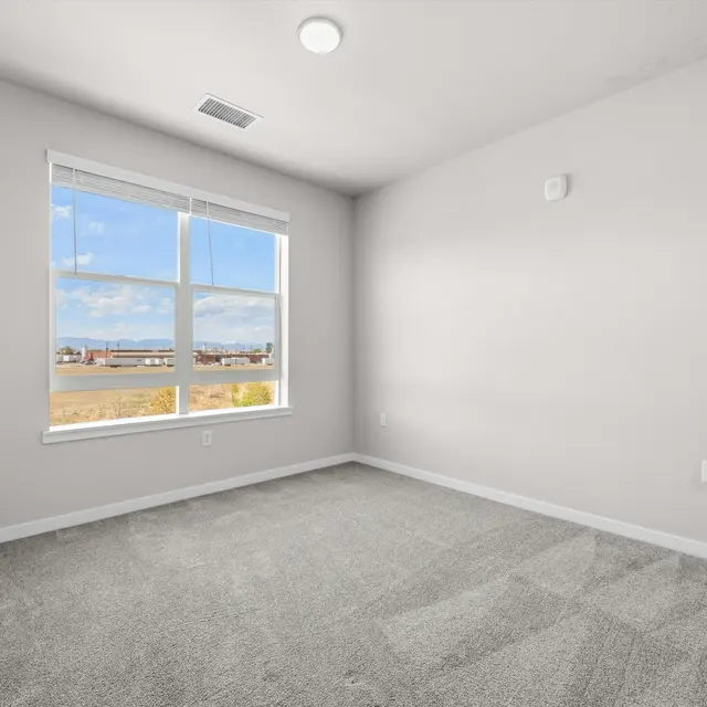 An empty room with gray carpet, a large window letting in natural light, and neutral-colored walls.