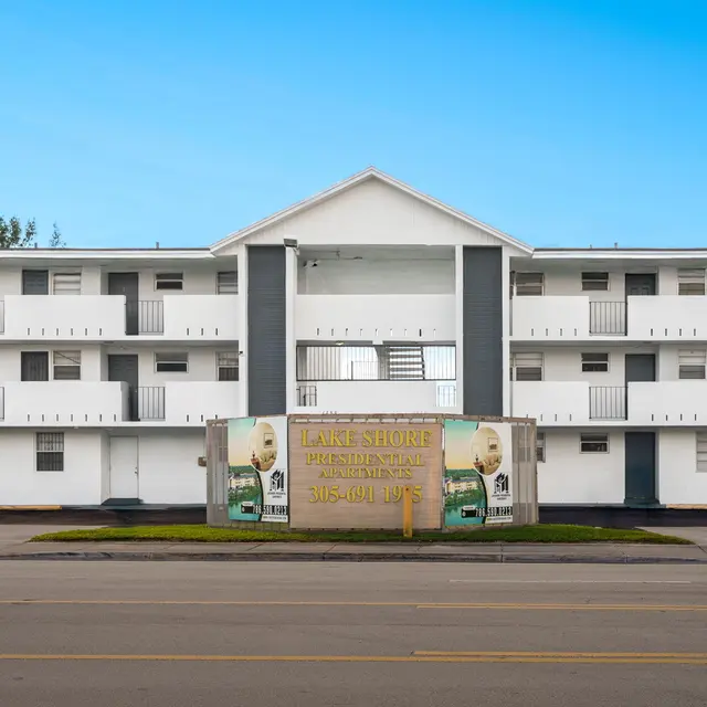 A two-story white motel-style building with a blue sky in the background, featuring multiple balconies and a large sign in front.