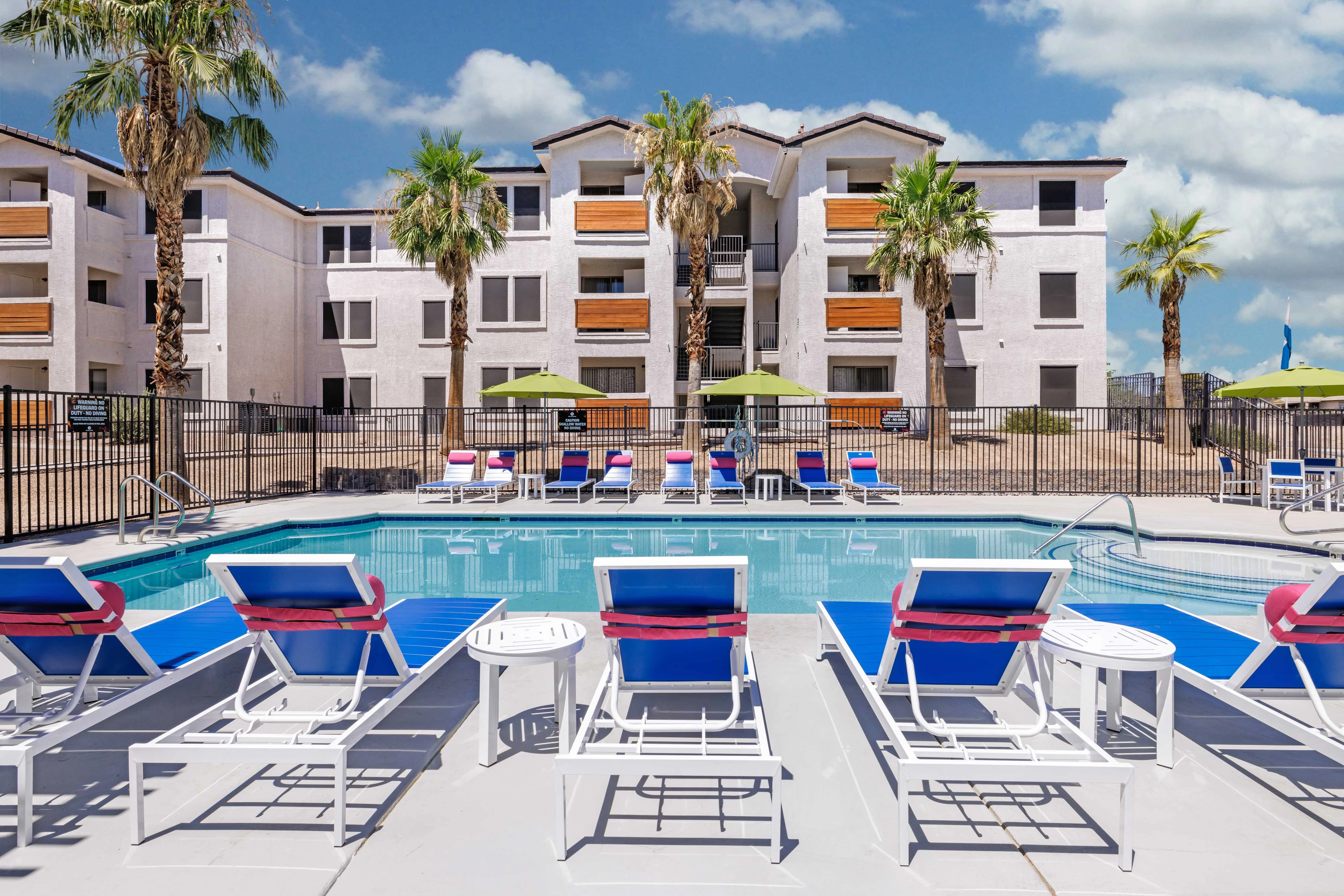 Apartment Pool Area Swimming pool surrounded by lounge chairs and palm trees with an apartment building in the background.