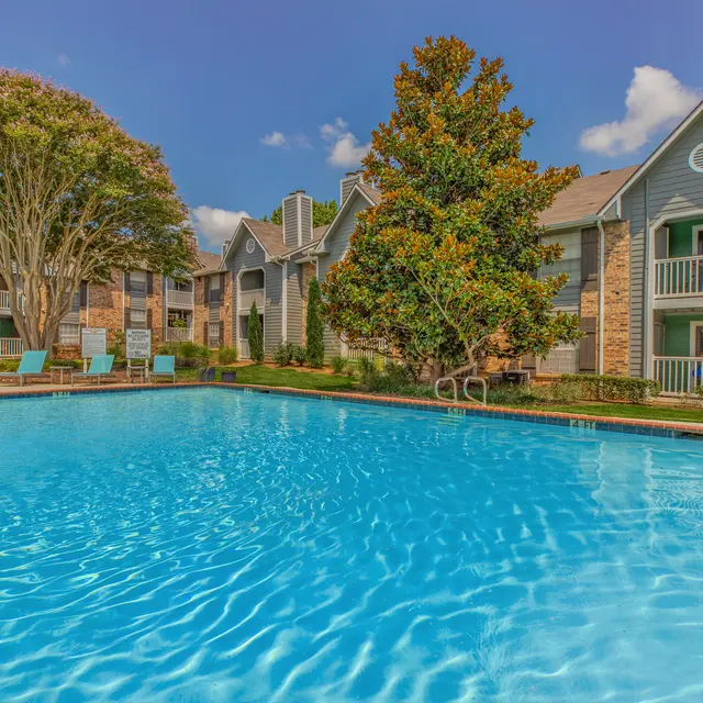 A clear blue swimming pool located in an apartment complex surrounded by greenery and residential buildings.