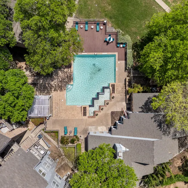 Aerial view of a swimming pool area surrounded by green trees and residential buildings.