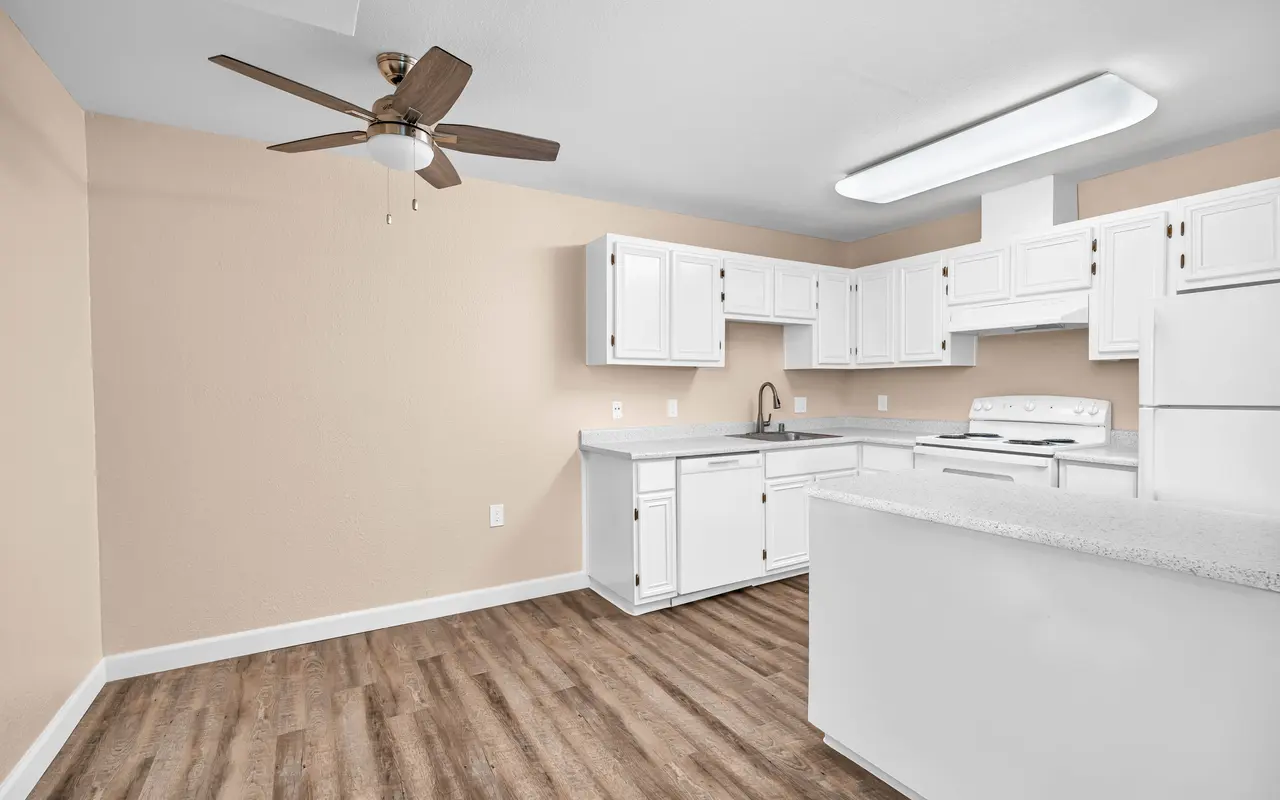 A modern kitchen featuring white cabinets, a ceiling fan, and wooden flooring. The space is well-lit with a neutral wall color, providing a bright atmosphere.