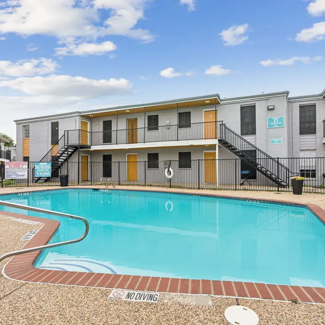 A clean swimming pool surrounded by a well-maintained apartment complex featuring two-story buildings with balconies and yellow doors.