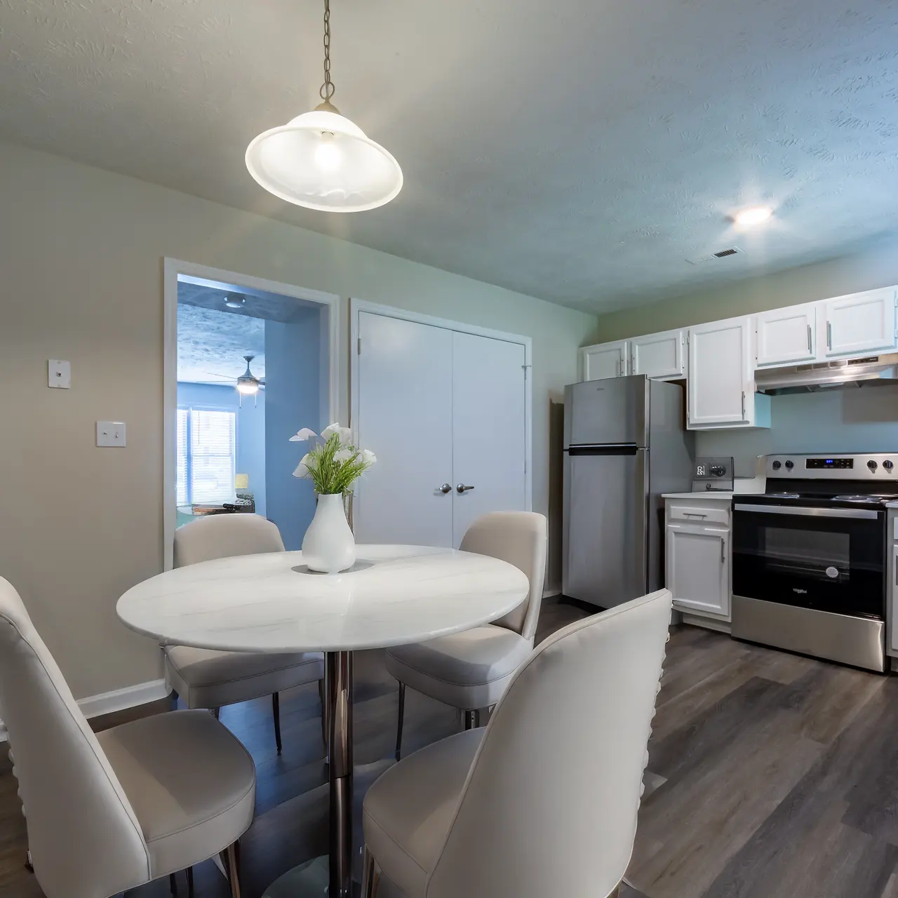 A modern kitchen featuring white cabinets, stainless steel appliances, and a round dining table with four upholstered chairs.