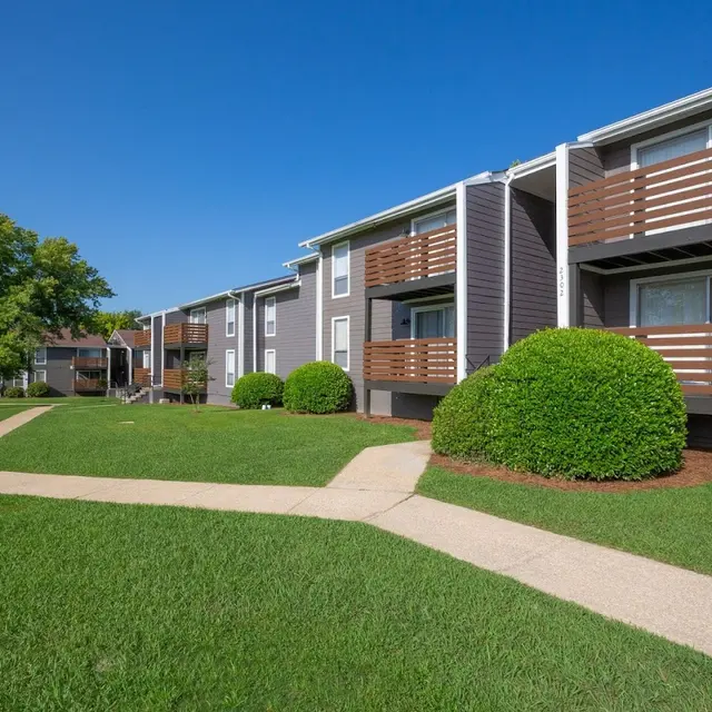 Exterior view of an apartment complex featuring multiple buildings with balconies and landscaped grassy area.