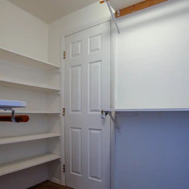 A minimalistic room featuring empty white shelves, an ironing board, and a door.