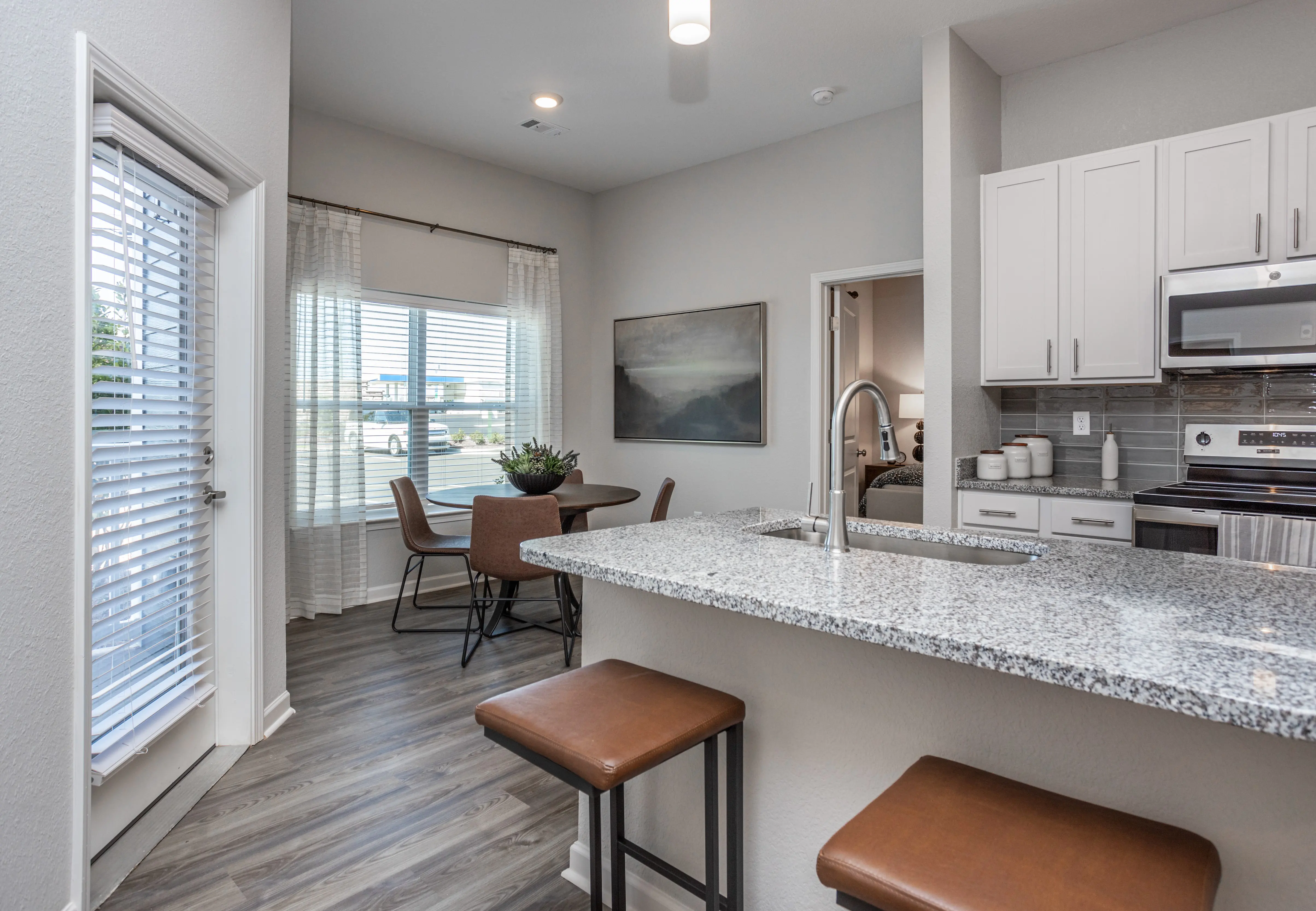 Stylish Kitchen and Dining Space A modern kitchen with a granite countertop, bar stools, and a dining area featuring a table and chairs, with natural light coming through the windows.