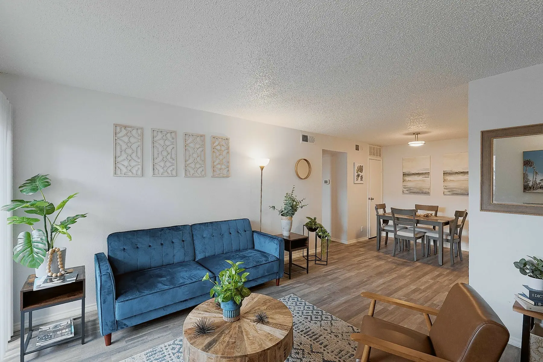 Cozy living room featuring a blue sofa, wooden coffee table, plants, and a dining area with modern decor and soft lighting.