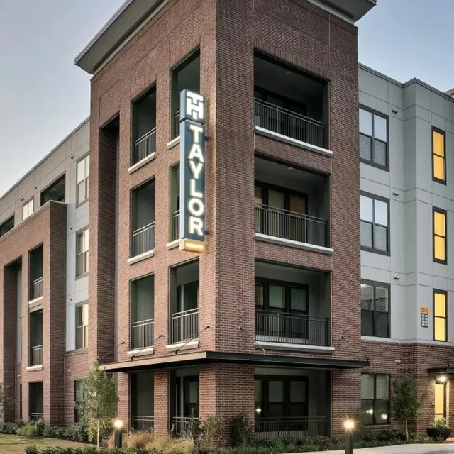SYNC Sawyer Heights Modern multi-story apartment building with a mix of brick and grey exterior, featuring balconies and large windows, illuminated at dusk.