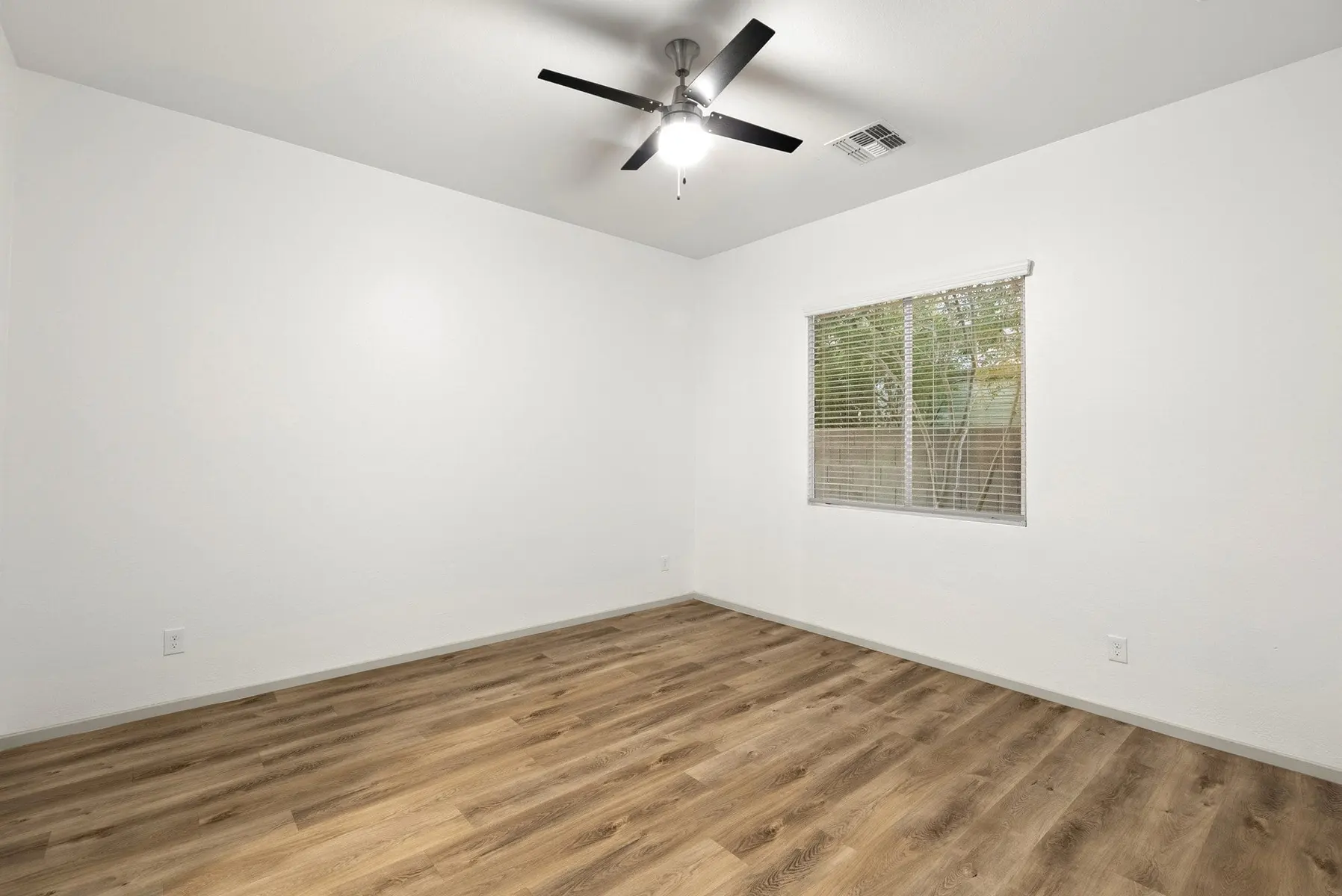 A blank room with light-colored walls, a ceiling fan, a window with blinds, and wood-like flooring.