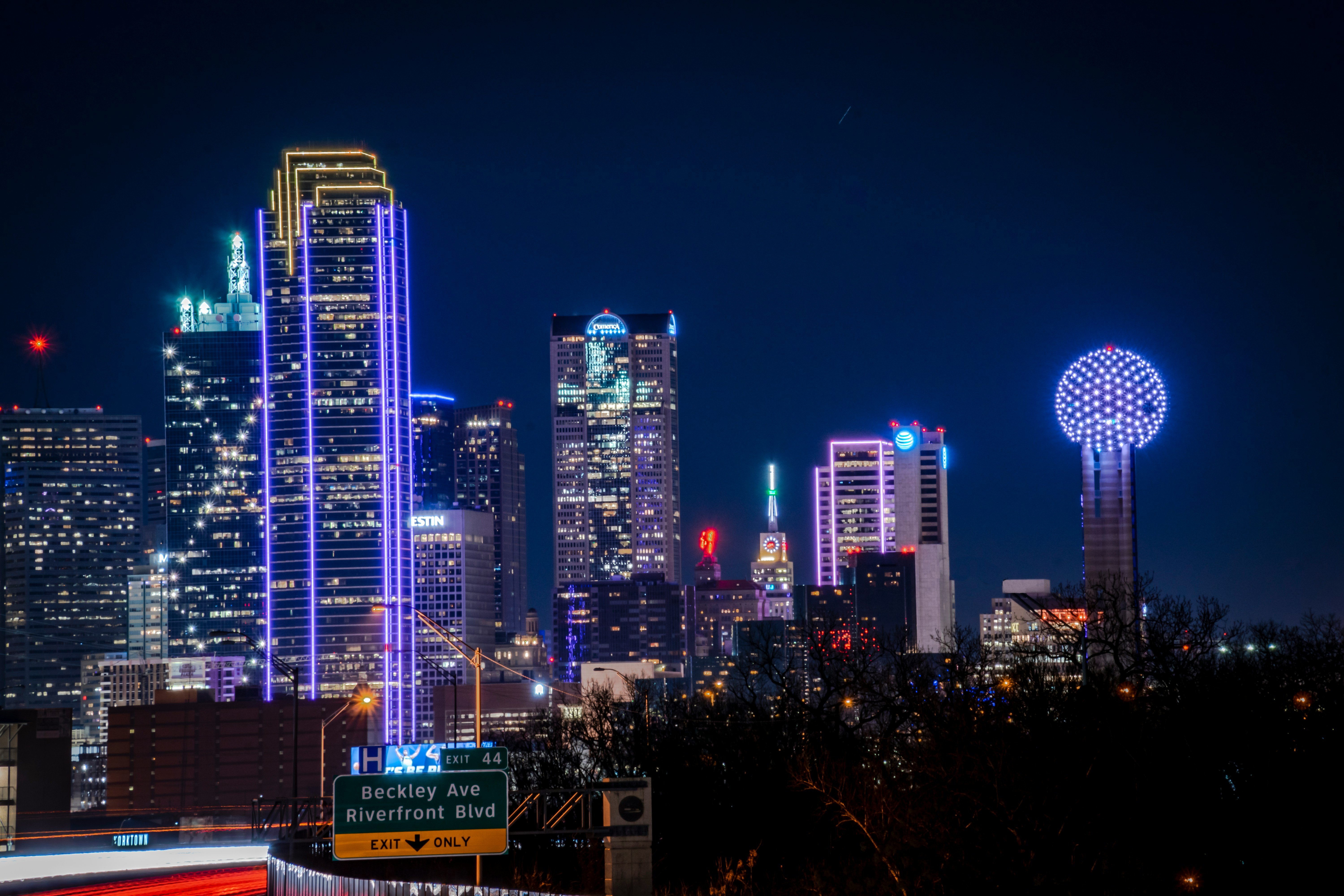 Night view of the Dallas skyline with illuminated skyscrapers and the iconic Dallas Observation Wheel.