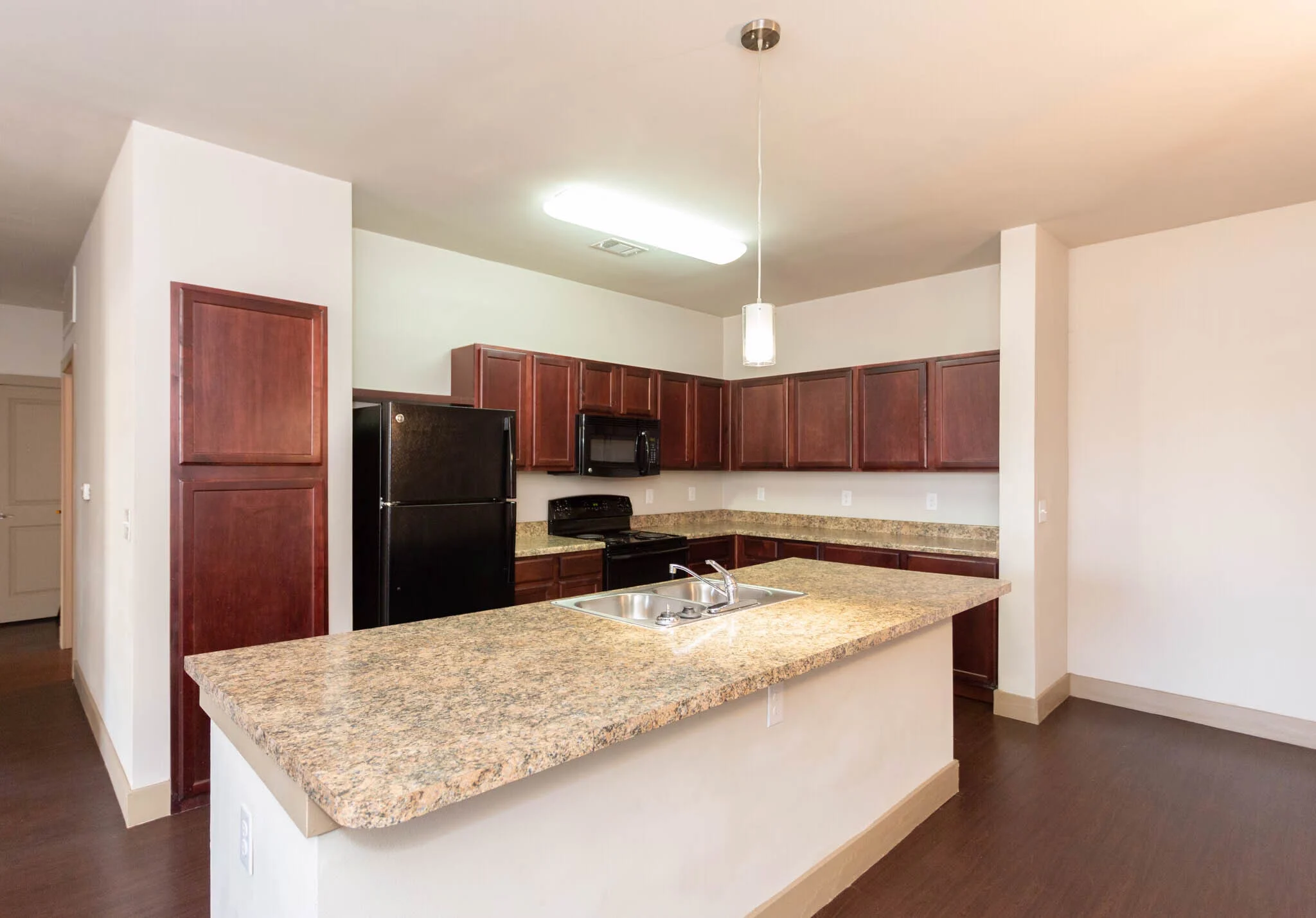Modern Kitchen Interior A spacious kitchen featuring dark wooden cabinets, a granite countertop island, black appliances including a refrigerator and oven, and ample natural light.
