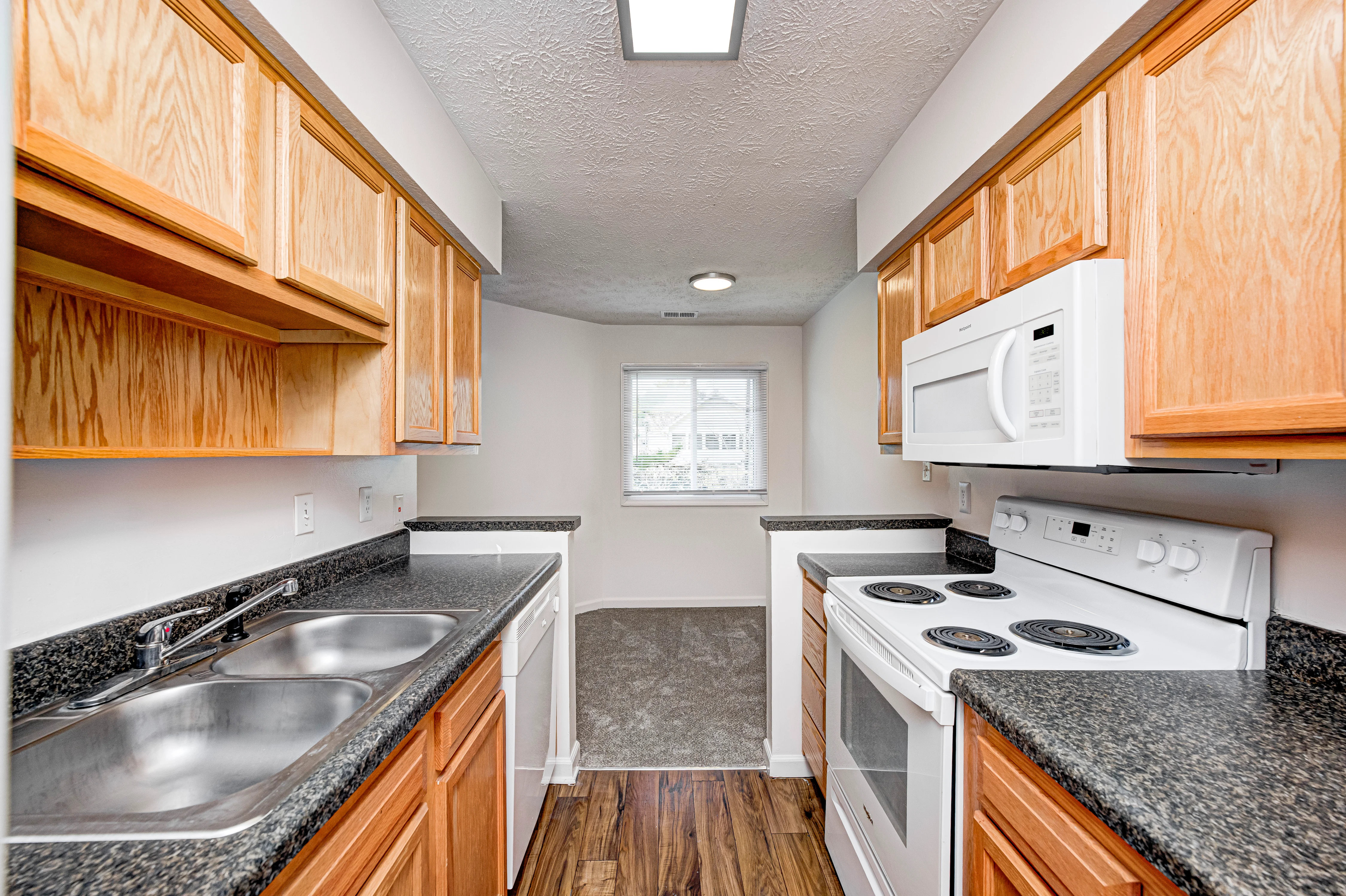 A modern kitchen featuring wooden cabinets, a double sink, and white appliances including a stove and microwave, with a window providing natural light.