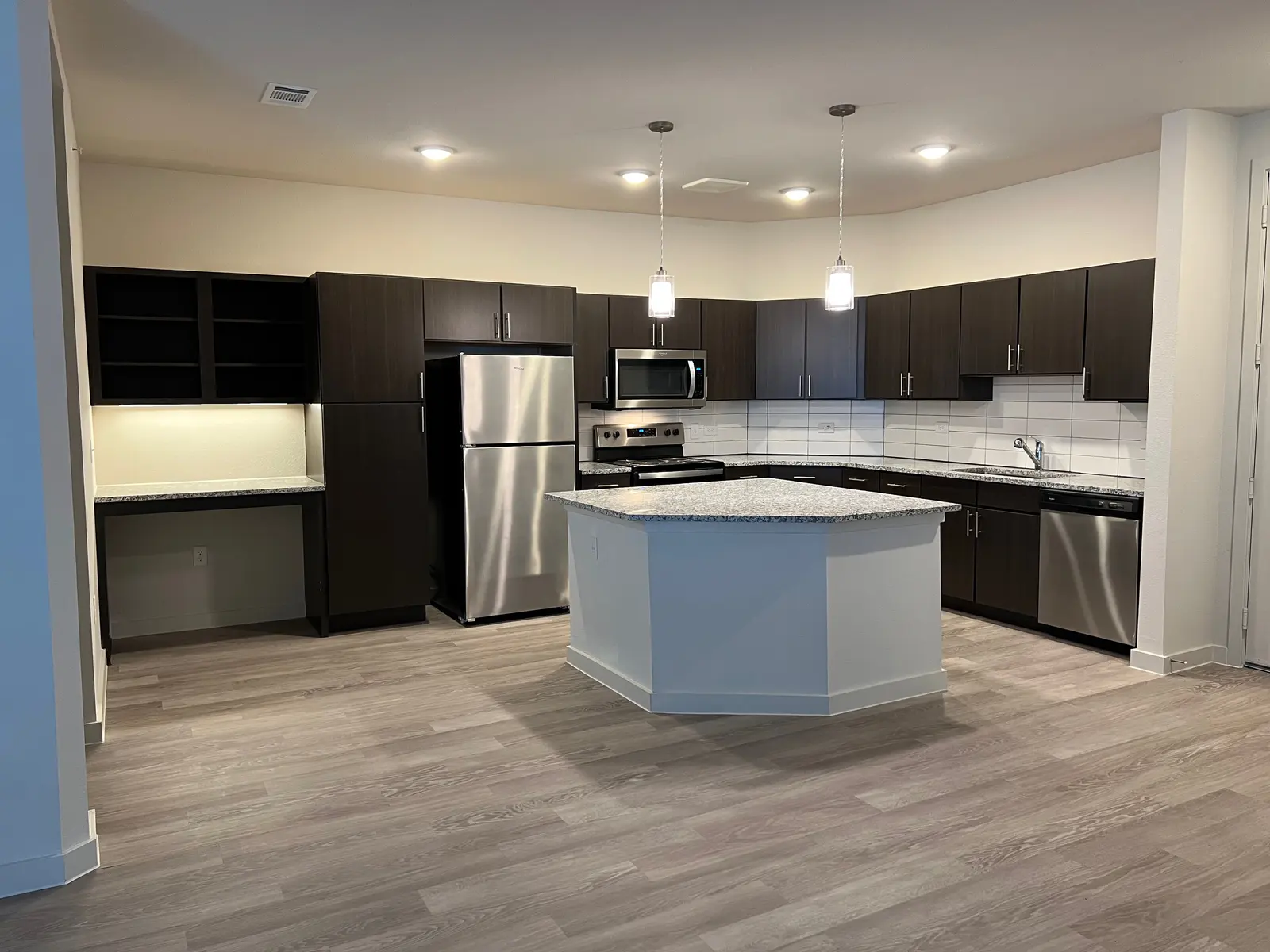 Modern Kitchen Aesthetic A modern kitchen featuring dark wood cabinets, stainless steel appliances, and an island countertop with a light marble finish. There are two pendant lights above the island and a light-colored tile backsplash.
