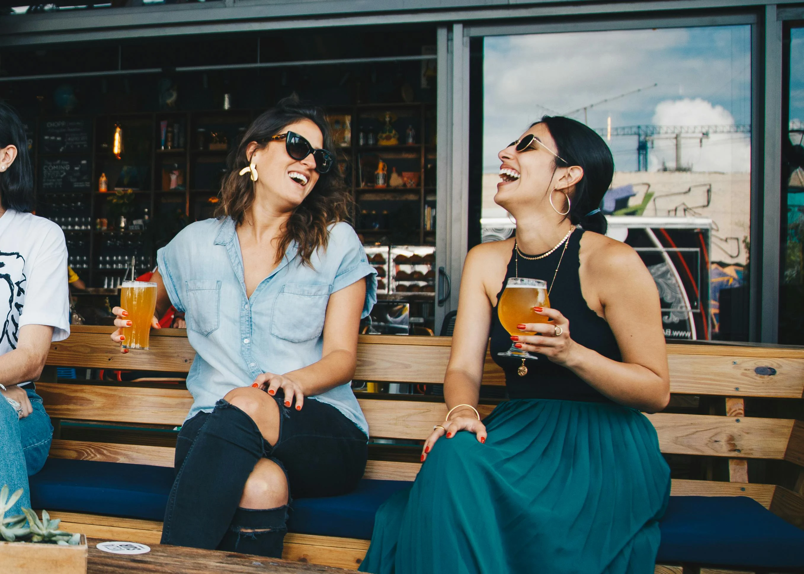 Friends Having Fun Two women sitting together, laughing and enjoying drinks in a casual setting.