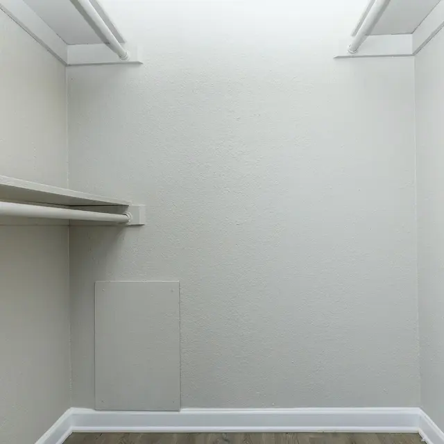 An empty closet with light gray walls, wooden flooring, and a small partition on one side.