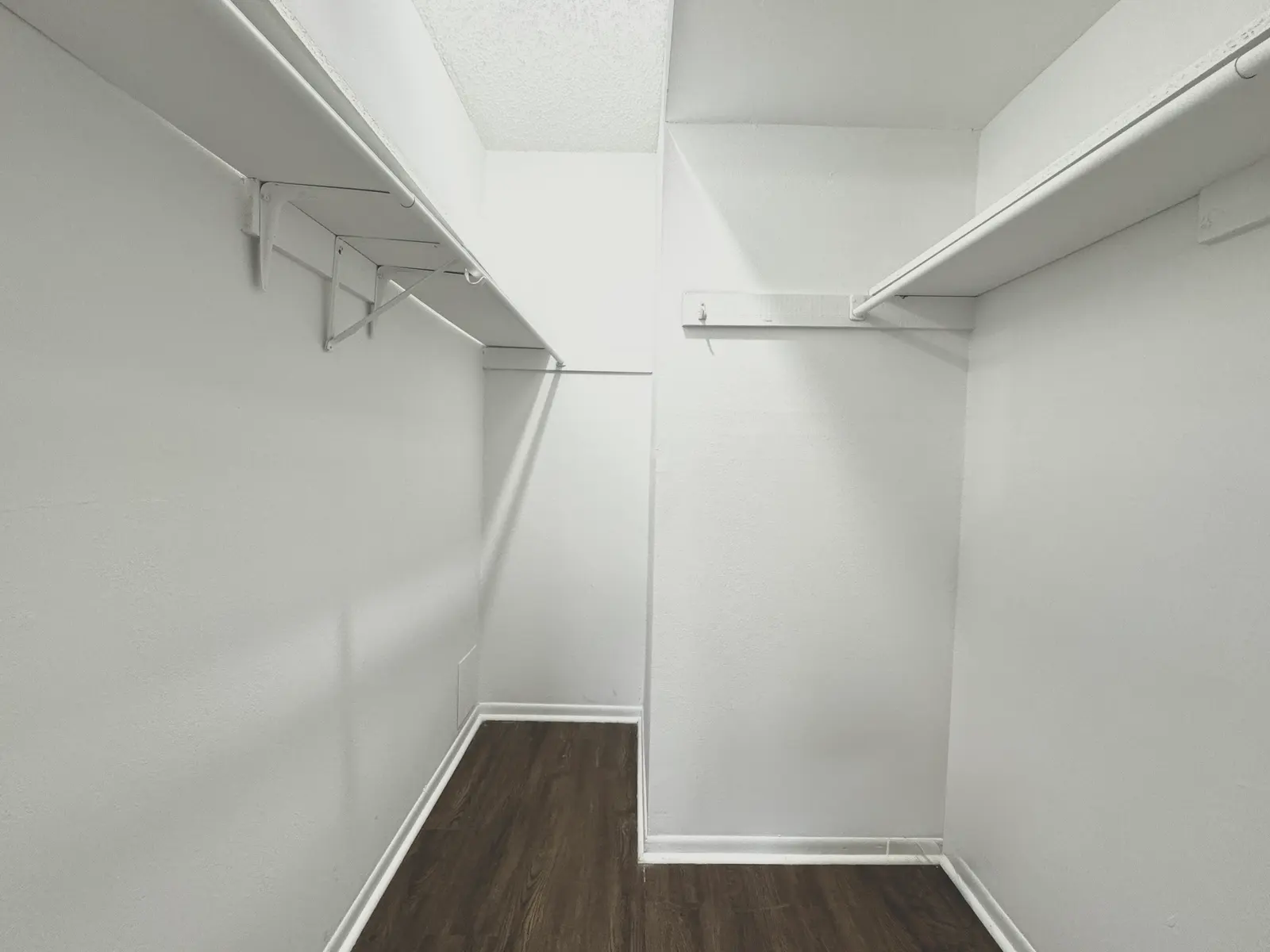 A spacious and empty walk-in closet with white walls and dark wooden floors.