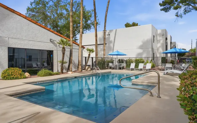 A tranquil pool area with clear blue water surrounded by patio furniture and palm trees.