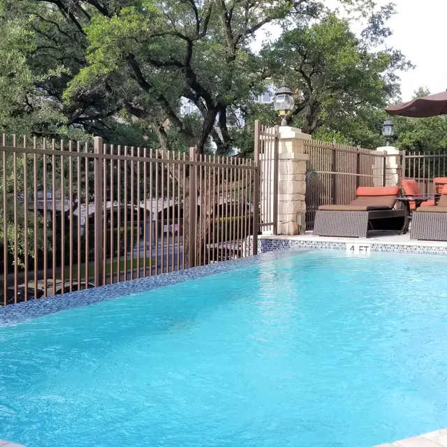A tranquil swimming pool area with a clear blue pool, lounge chairs, and shaded seating under umbrellas, surrounded by greenery.