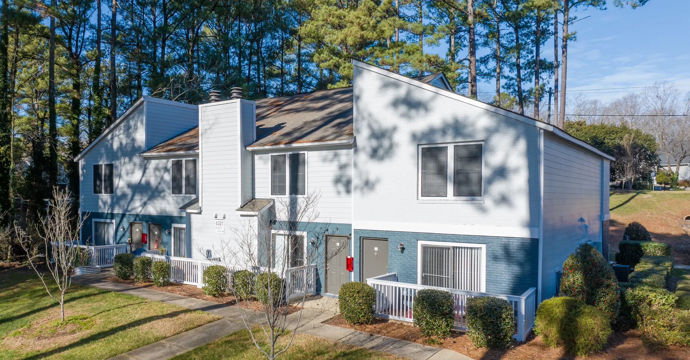 Exterior view of a residential building surrounded by trees, showcasing a two-story structure with multiple units.