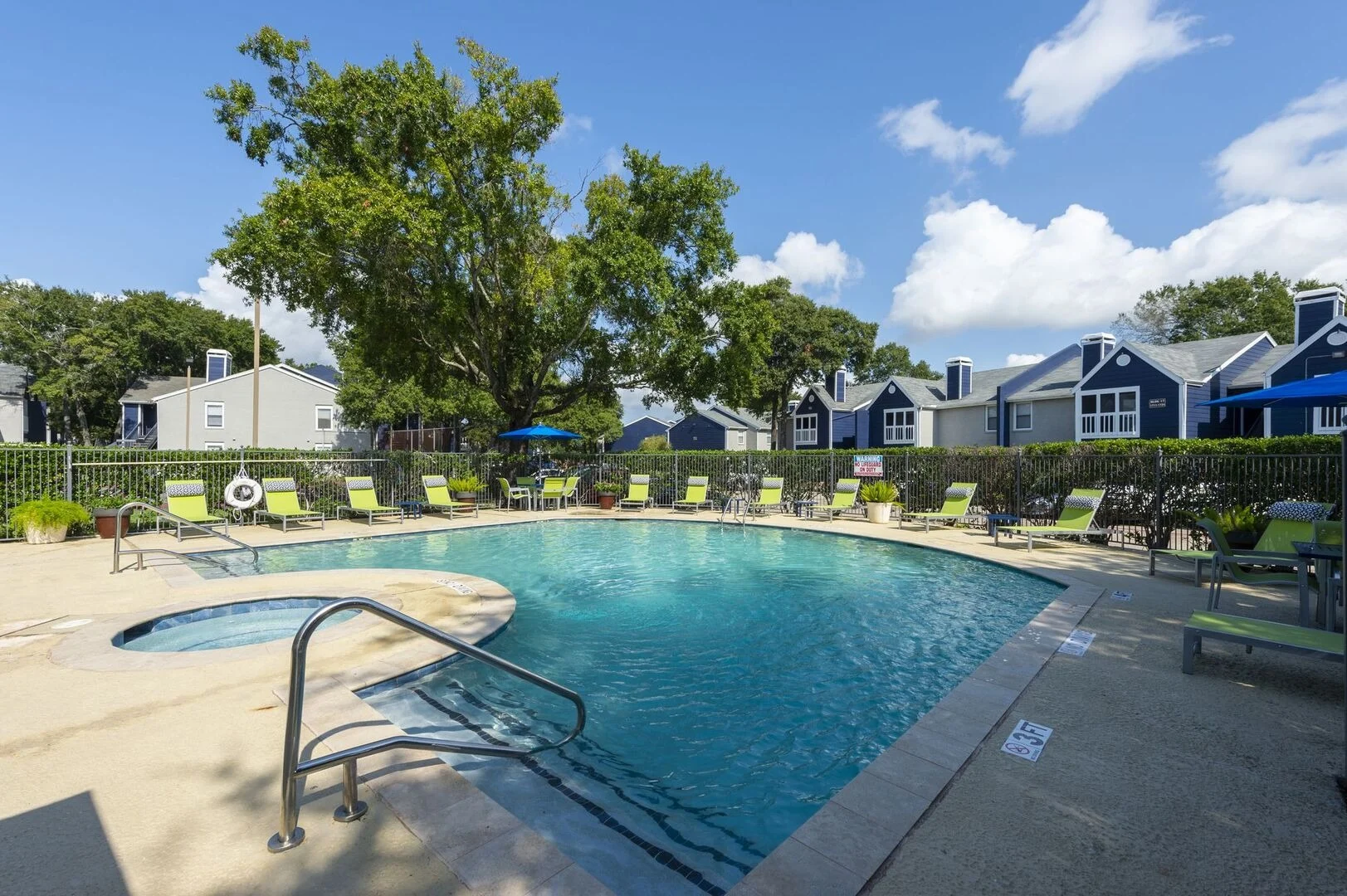 A swimming pool surrounded by lounge chairs and green grass under a blue sky with clouds.