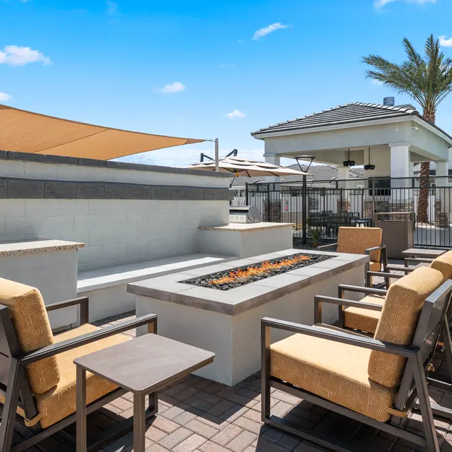 Cozy outdoor seating area with fire pit, surrounded by palm trees and shaded by umbrellas, near a residential building.