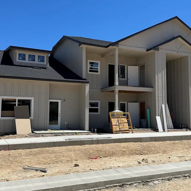 Newly Constructed House Front view of a new, unfinished two-story house with light-colored siding and a dark roof under a clear blue sky.