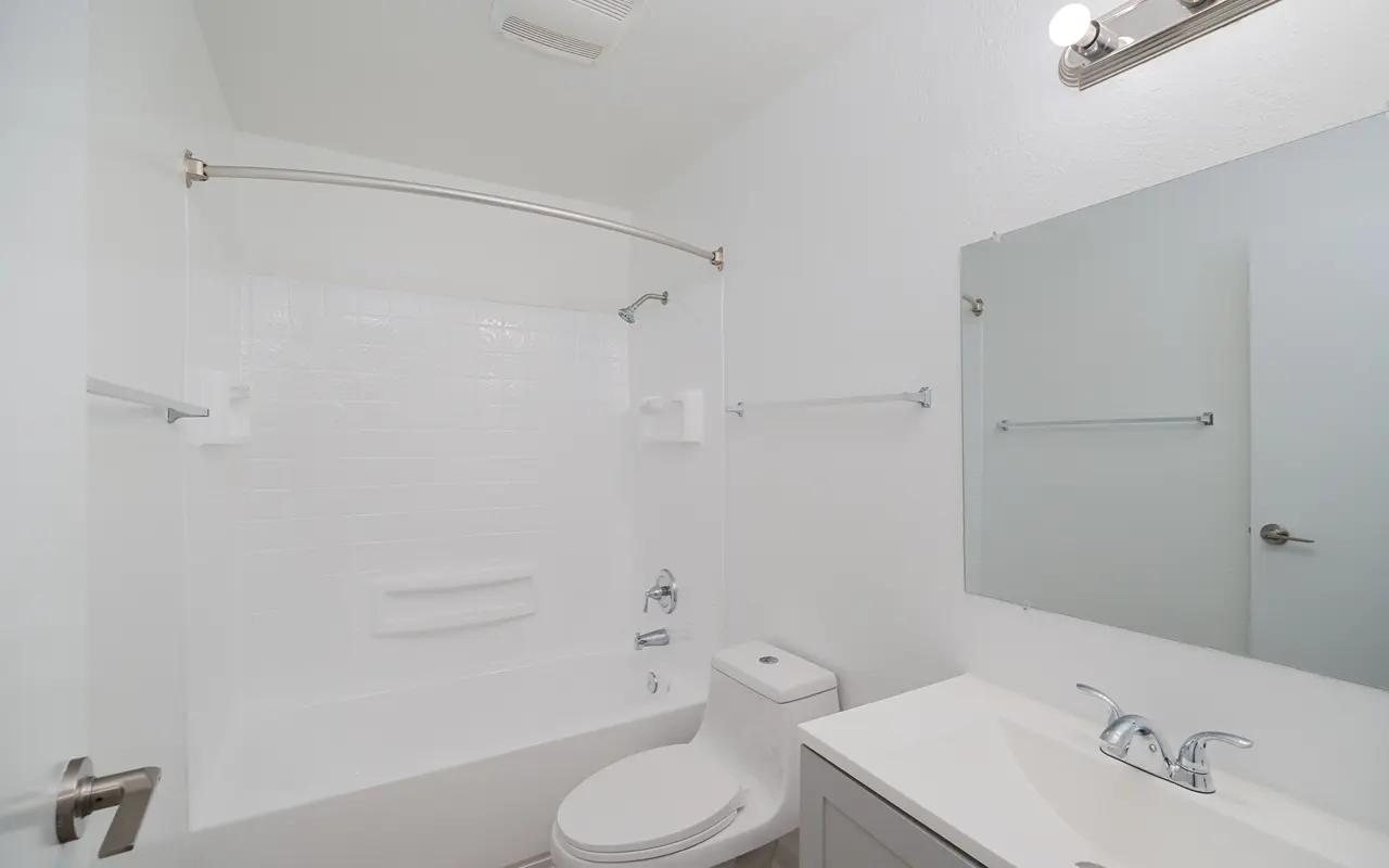 A clean and modern bathroom featuring a shower/tub combo, a toilet, and a sink with a vanity. The walls are painted white, providing a bright atmosphere, while the design is minimalist with simple fixtures.