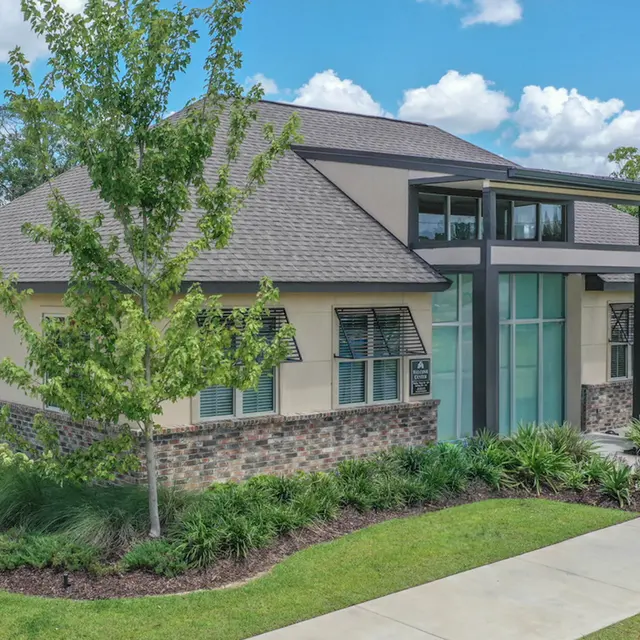 A contemporary single-story building with a modern design, featuring a mix of beige stucco and stone elements, large windows, and a landscaped yard.