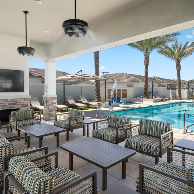 Modern poolside area featuring comfortable seating, a TV, and palm trees, with a clear blue sky above.
