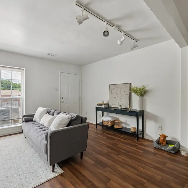 Modern Living Room Interior A bright and modern living room featuring a gray sofa, a white rug, and a minimalist console table against a white wall. Large windows provide ample natural light.