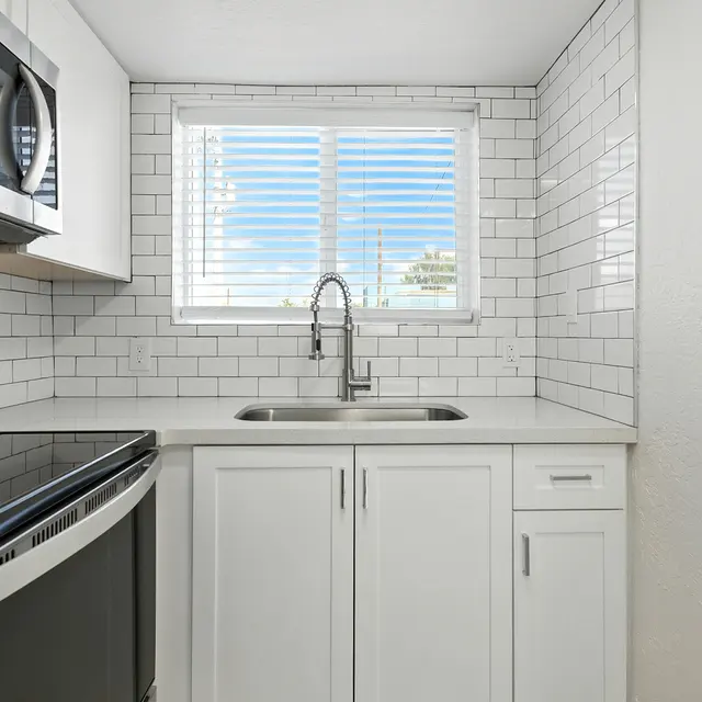 A modern kitchen featuring white subway tile backsplash, stainless steel appliances, and a sink beneath a window with horizontal blinds.