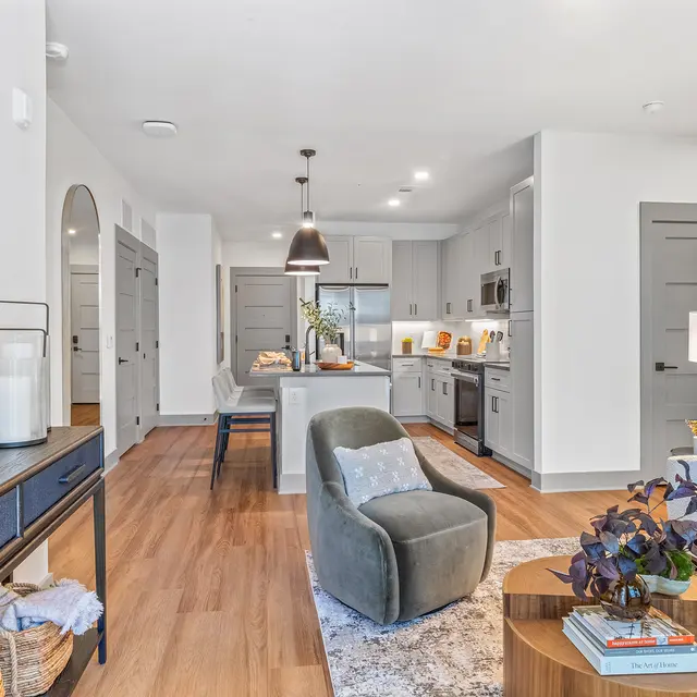 A modern living area featuring a cozy couch, a coffee table, a stylish armchair, and a kitchen view in the background.