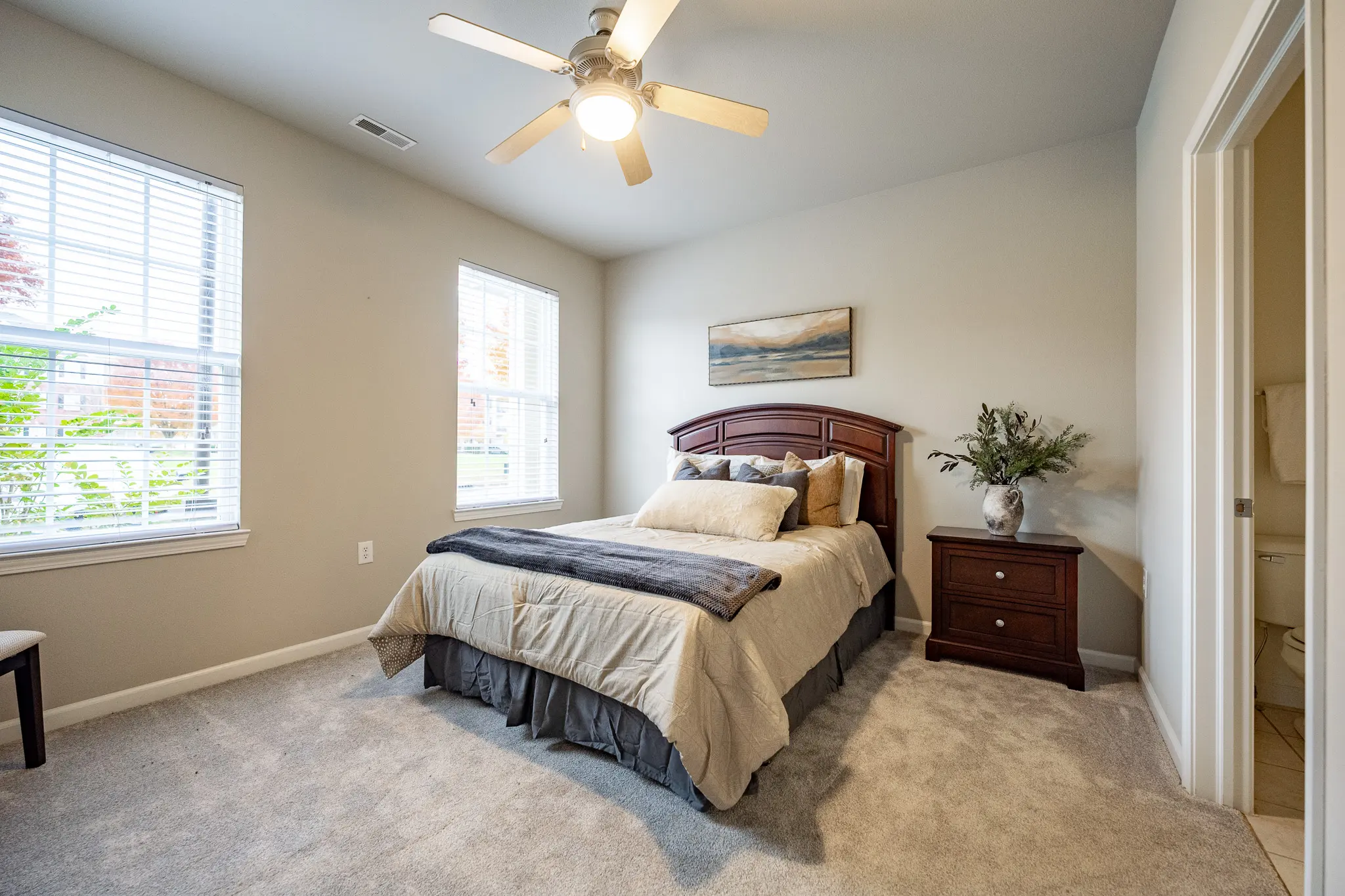 A cozy bedroom featuring a bed with a decorative comforter, a bedside table, and windows allowing natural light.