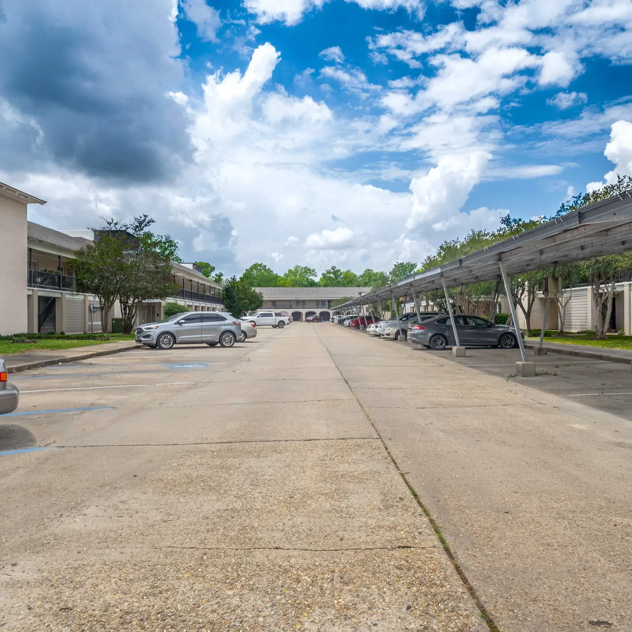 A view of a parking lot in an apartment complex with several parked cars and a clear blue sky in the background.