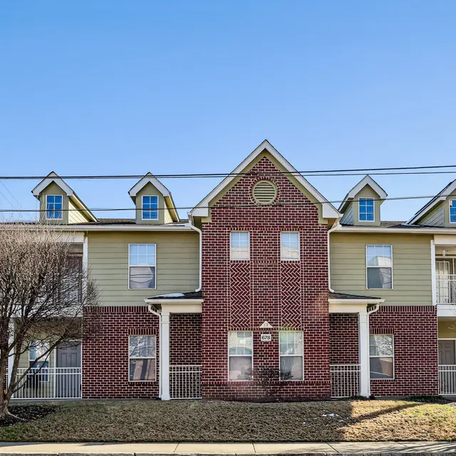 Two-Story Apartment Building A front view of a two-story apartment building with a combination of yellow and red brick exterior, featuring a gabled roof and multiple windows.