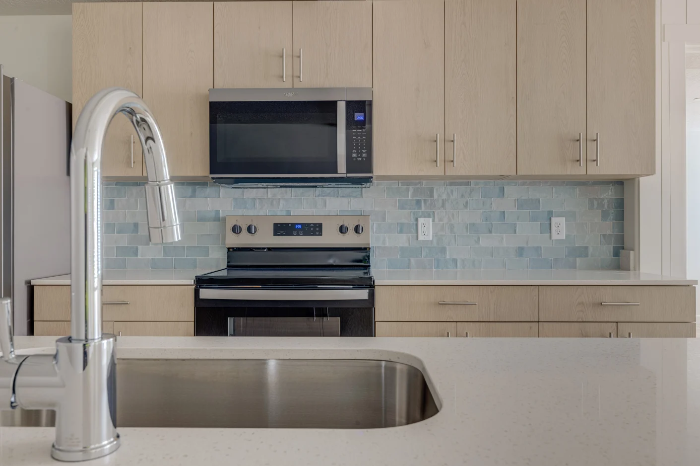 Stylish Modern Kitchen A modern kitchen featuring light wood cabinetry, a stainless steel microwave, and a sleek countertop with a visible sink faucet.