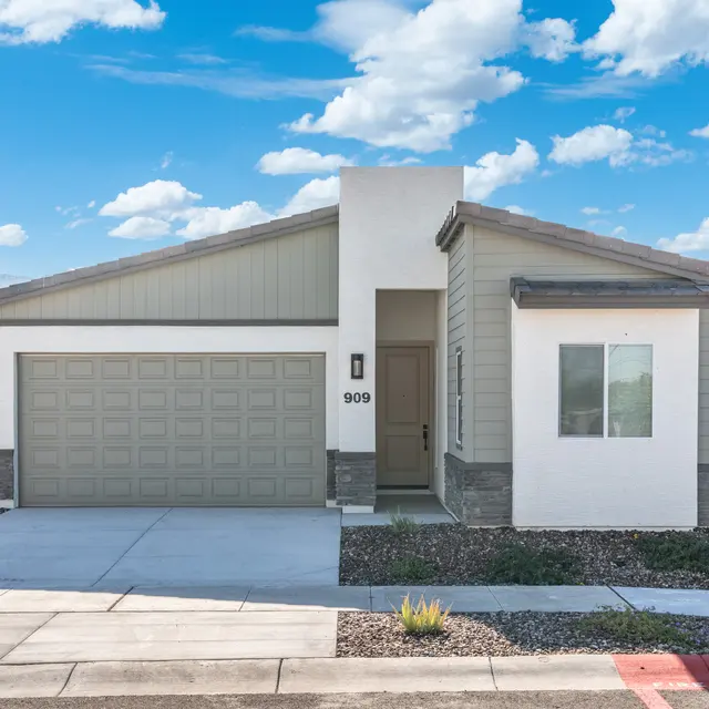 A modern single-story house with a light-colored facade and a two-car garage, situated on a clear day under a blue sky with clouds.