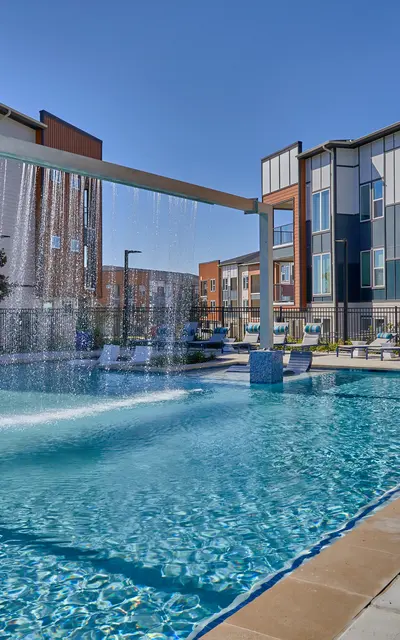 A modern luxury apartment complex featuring a swimming pool with a waterfall feature and lounge chairs.