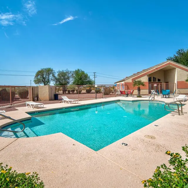 Outdoor swimming pool area with lounge chairs and surrounding greenery under a clear blue sky.
