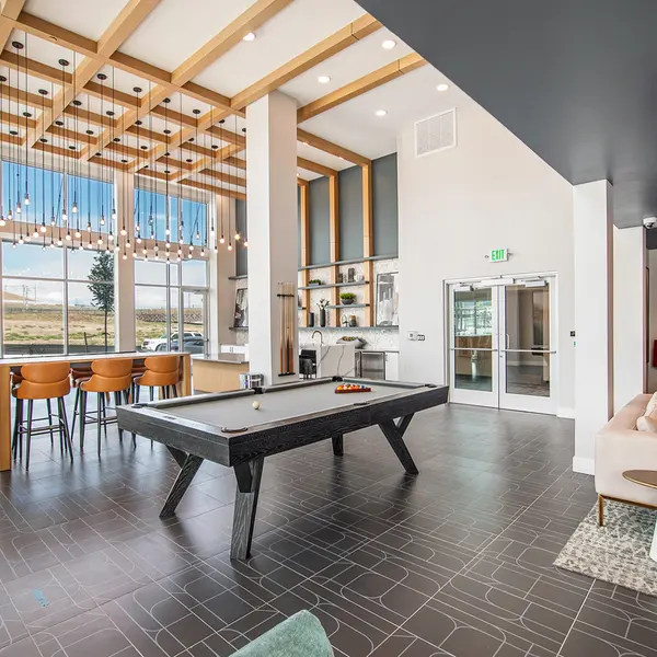 Modern lounge area featuring a pool table, bar seating, and large windows with natural light, stylish decor, and a cozy ambiance.