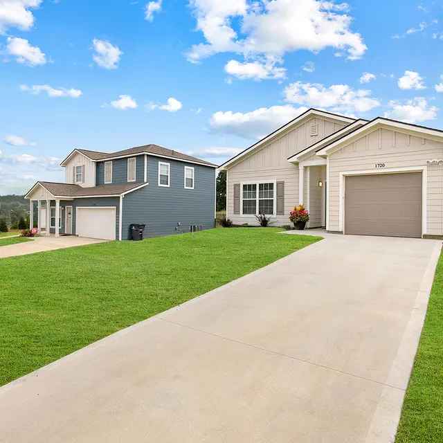 Two modern homes in a suburban neighborhood with a clear blue sky and green lawn.