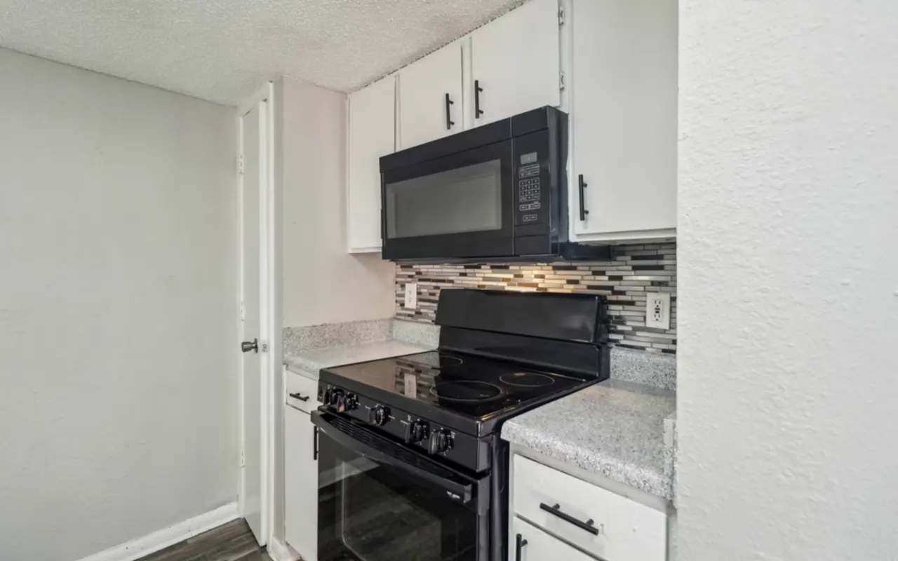 A modern kitchen featuring a black stove and microwave, alongside white cabinets and a stylish backsplash.