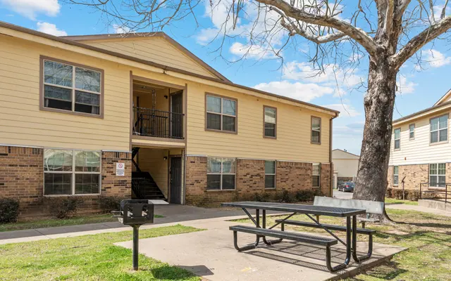Apartment Complex Outdoor View Exterior view of an apartment complex with a picnic table in the foreground and a large tree nearby.