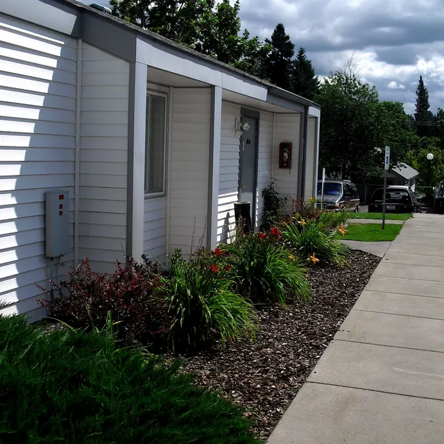 Residential Building with Pathway A well-maintained residential building featuring white siding and a pathway lined with greenery and flowers.