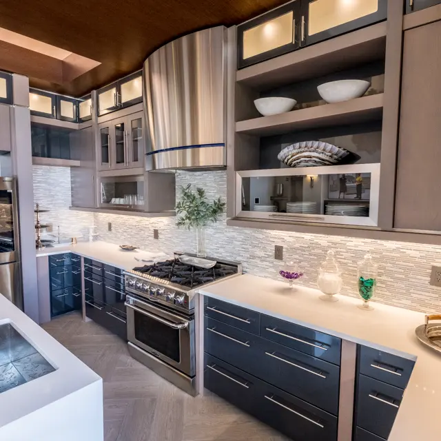 A modern kitchen with dark cabinets, stainless steel appliances, and a large kitchen island. The kitchen has a sleek design with under-cabinet lighting and decorative dishware on shelves.