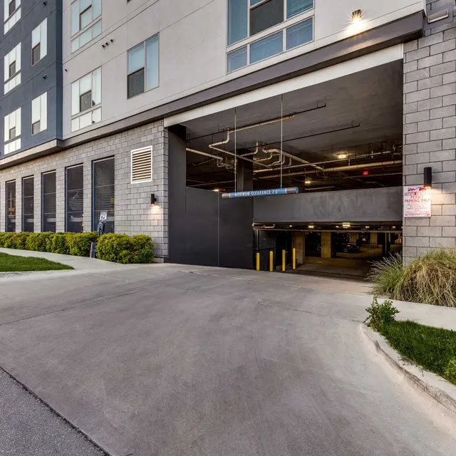 Entrance to a modern apartment building's parking garage with greenery along the pathway.