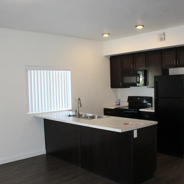 Modern Kitchen Design A modern kitchen with dark wood cabinetry and black appliances, featuring a white countertop and a sink on a kitchen island, with a window providing natural light.